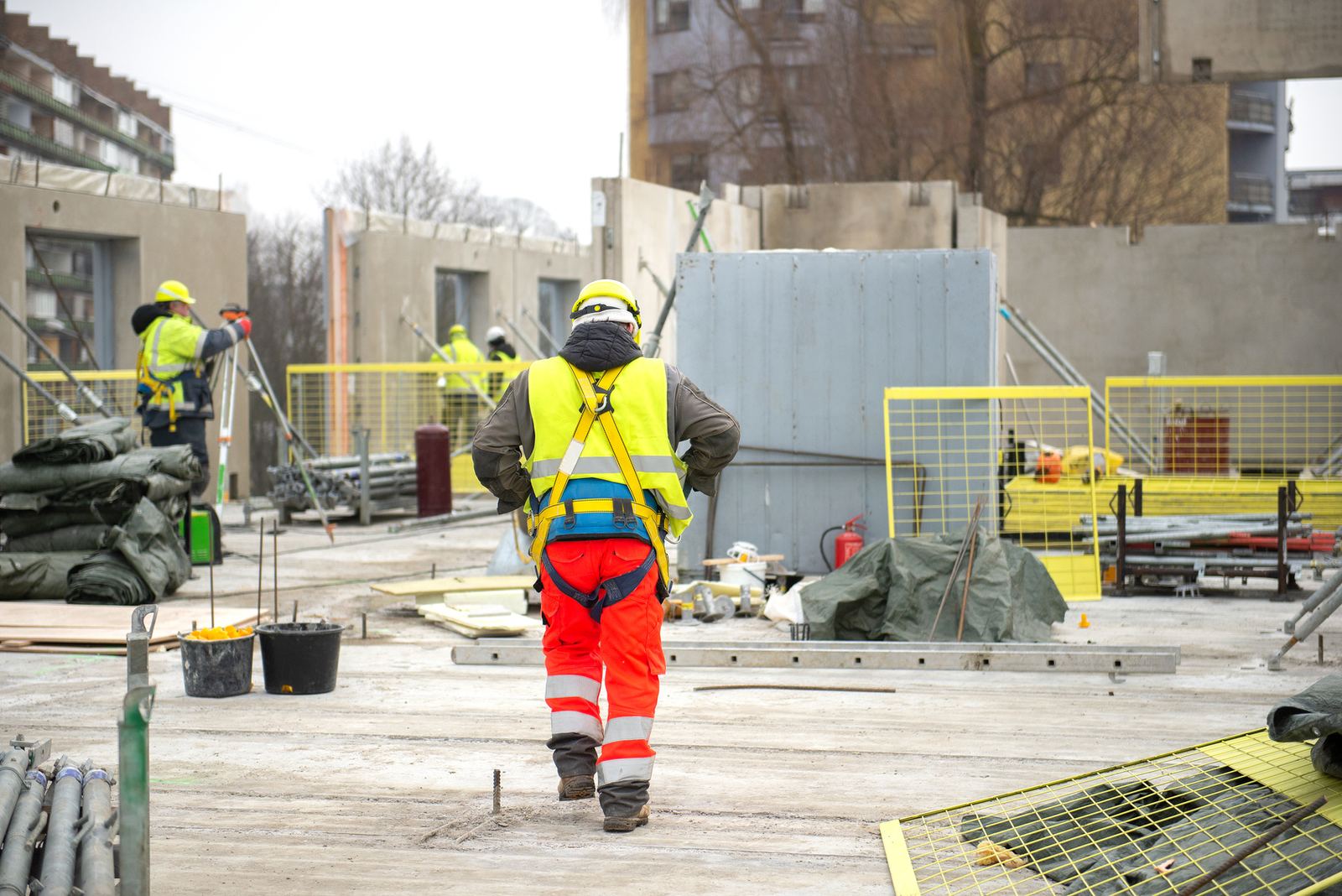 A construction worker in a hard hat and hi-vis vest on a building site, seen from behind